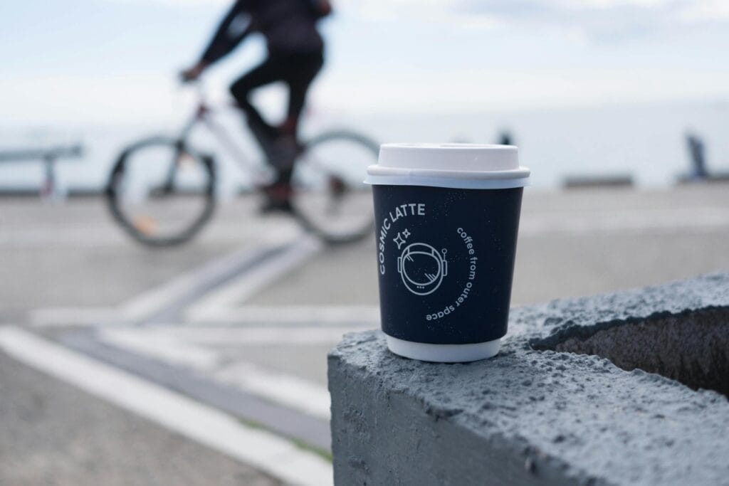A plastic coffee cup on a concrete block by the sea with a blurred cyclist in the background.